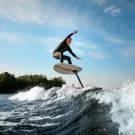 young athletic man in black wetsuit balancing on a foilboard on a wave on a sunny day