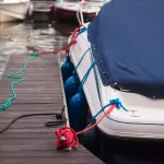 a modern motor boat windshield and bow deck covered in a blue canvas rain cover, with a weathered wood dock and blurry port in background
