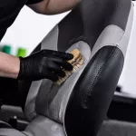 Man car wash worker cleaning leather boat seat with brush and detergent
