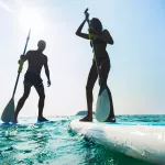 Stand up paddle board couple paddleboarding . Young caucasian couple on Thailand beach on summer holidays vacation travel.