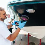 Boat maintenance - Man with orbital polisher polishing boat in marina. Selective focus.