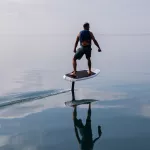 Man riding an electric hydrofoil foil board on a lake with a life jacket