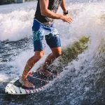 Active wakesurfer jumping on wake board down the river waves. Surfer on wave. Male athlete training on wakesurf training. Active water sports in open air on board. A man catches a wave on surf.